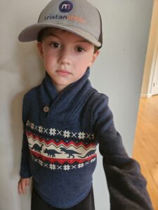 Boy wearing dinosaur sweater and hat.